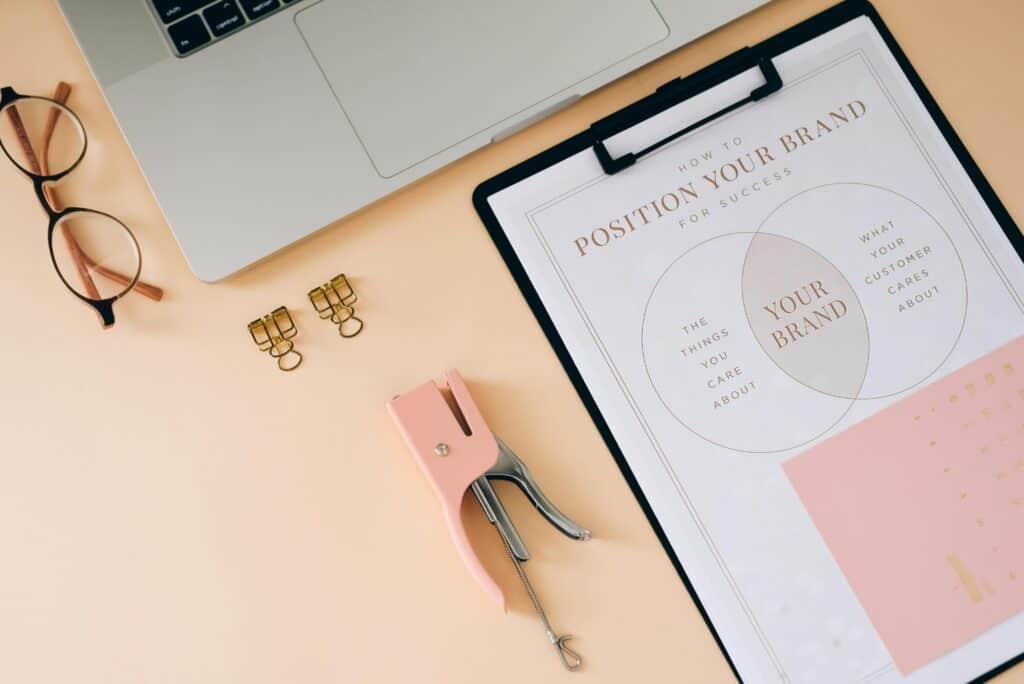 Flat lay workspace illustrating B2B messaging and positioning for professional services with a laptop, glasses, and a brand strategy clipboard.